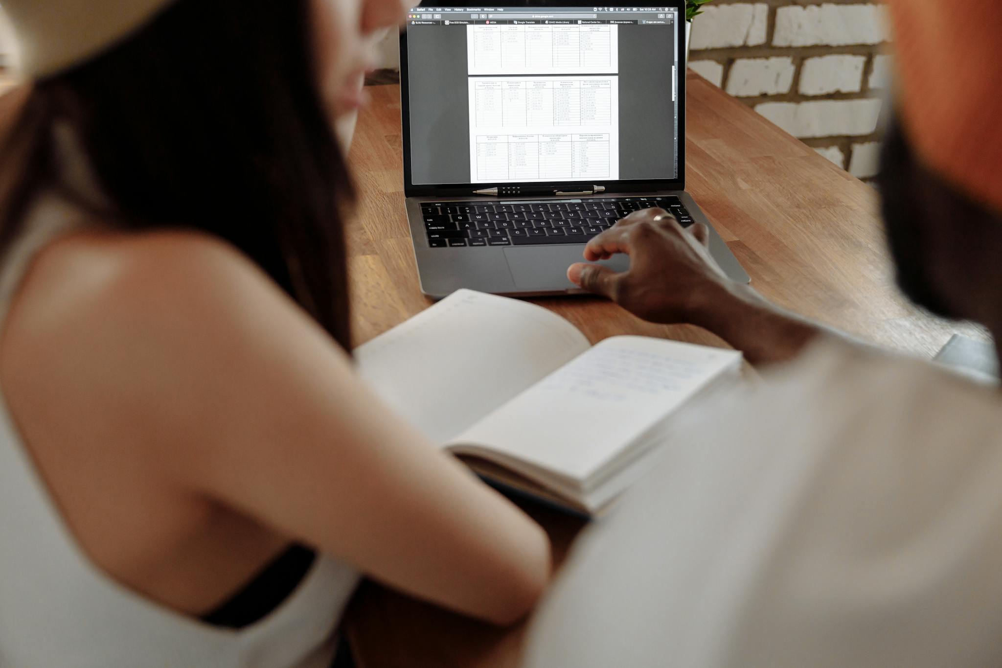 Two young adults collaborating in a home office setting with laptop and notebook.